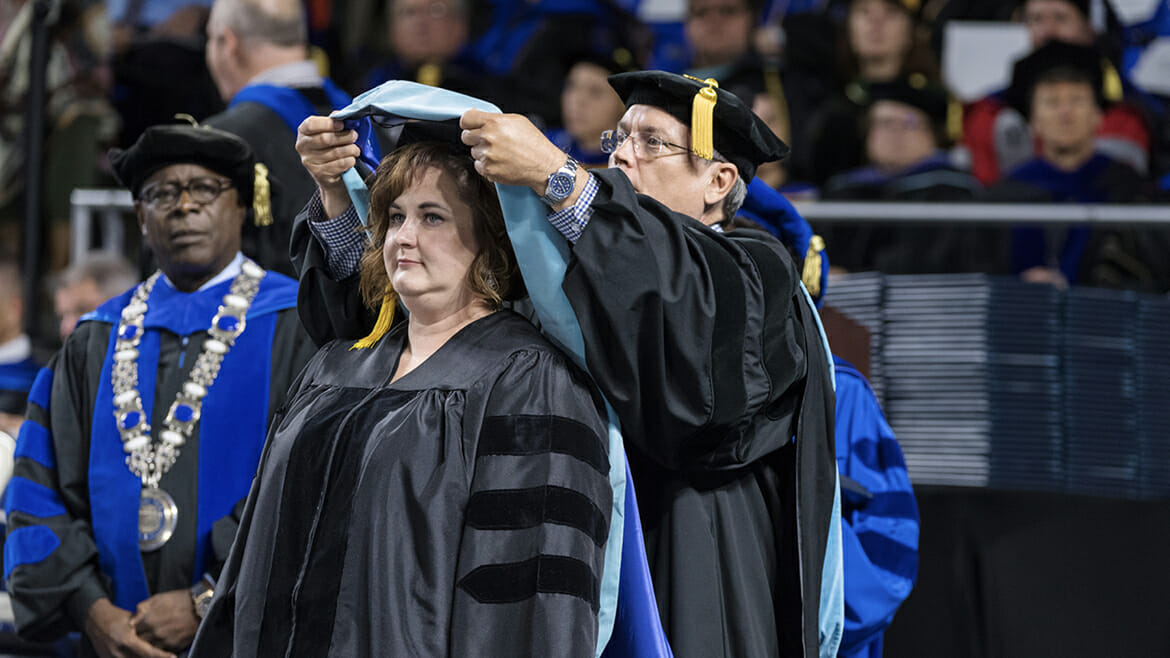 Newly minted doctoral degree holder Kelli Roberts Seymour, center, stands as MTSU College of Education professor Terry Goodin carefully places the hood signifying completion of her Doctor of Education in Assessment, Learning and School Improvement around her neck at the May 2017 College of Graduate Studies commencement ceremony in Murphy Center. Looking on at left is MTSU President Sidney A. McPhee. Seymour is principal of Theodore Roosevelt Elementary School in Kingsport, Tenn., and completed her dissertation on “Shared Leadership, Professional Learning Communities, and Teacher Self-Efficacy: How One Impacts the Other.” (MTSU photo by Andy Heidt)