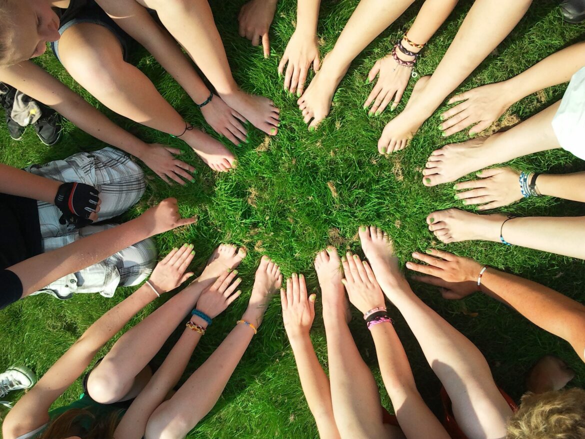 A group of people are sitting in the grass with their hands and feet making a circle.