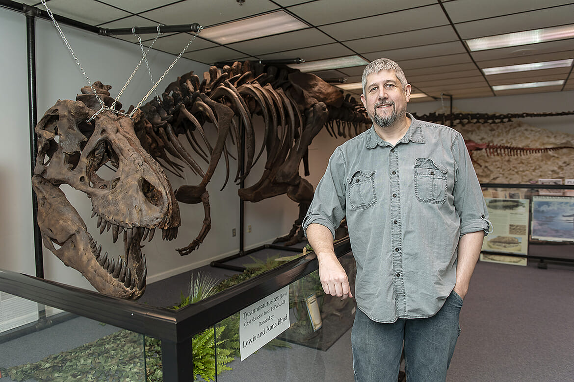 Alan Brown, a geosciences lecturer at MTSU, poses with a full-sized replica of a T. rex dinosaur at the Earth Experience natural history museum in Murfreesboro. (MTSU photo by Andy Heidt)