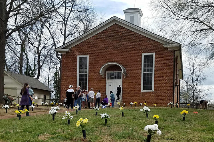 Visitors gather outside St. Philips Moravian Brick Church in the village of Old Salem in Winston-Salem, North Carolina, to prepare for the African-American Heritage Tour that traces the history of one of the oldest black congregations in the United States. The flowers mark the burial places revealed by archaeological excavations of Salem’s original Strangers’ Graveyard and the graveyard used for enslaved African-Americans after their white Moravian neighbors embraced racial segregation. MTSU history and animation students will be working together this summer to bring the 19th-century site back to 3D life. (Photo courtesy of the Old Salem Museum and Gardens)