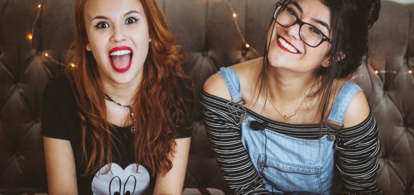 Photo of two women sitting on a couch smiling. Photo by Matheus Ferrero on Unsplash.