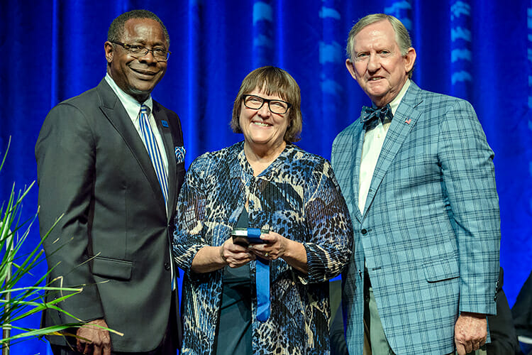 MTSU chemistry professor and nationally recognized STEM education advocate Judith Iriarte-Gross, center, proudly accepts the 2018 MTSU Foundation Career Achievement Award Thursday, Aug. 23, from MTSU President Sidney A. McPhee, left, and MTSU Foundation President Ron Nichols, right, at the university's Fall Faculty Meeting inside Tucker Theatre. Iriarte-Gross, who's taught at MTSU since 1996, is director of the Women In STEM (WISTEM) Center at MTSU and the founder and director of Tennessee’s first Expanding Your Horizons girls’ science, technology, engineering and math education workshop. The Career Achievement Award is presented annually to a professor at MTSU and is considered the pinnacle of recognition for the university's faculty. Iriarte-Gross also is a fellow of both the American Chemical Society and the American Association for the Advancement of Science, two of the country's premier scientific professional societies, among her many honors. (MTSU photo by J. Intintoli)