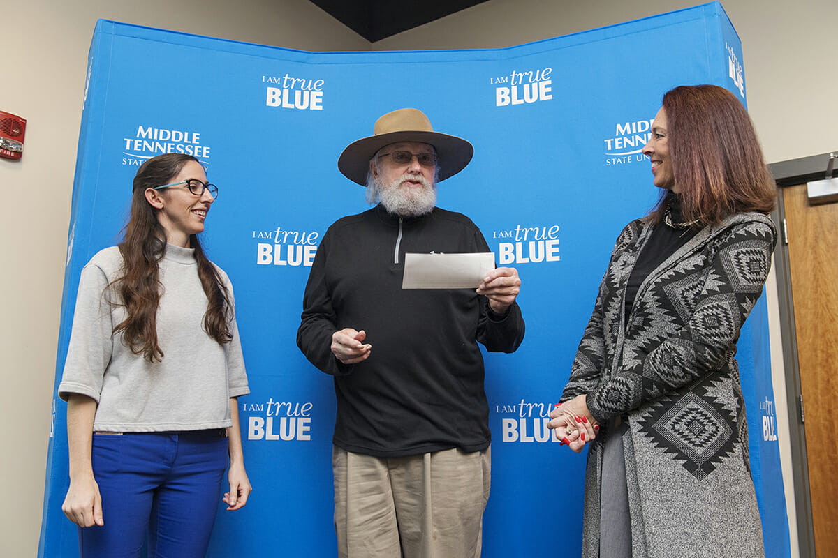 Charlie Daniels, center, accepts a $1,000 check for his nonprofit Journey Home Project from Rochelle Cintron with Optum.