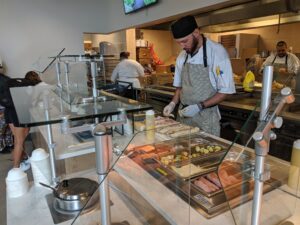 A cook works on the daily sandwich in front of students with locally sourced ingredients. 