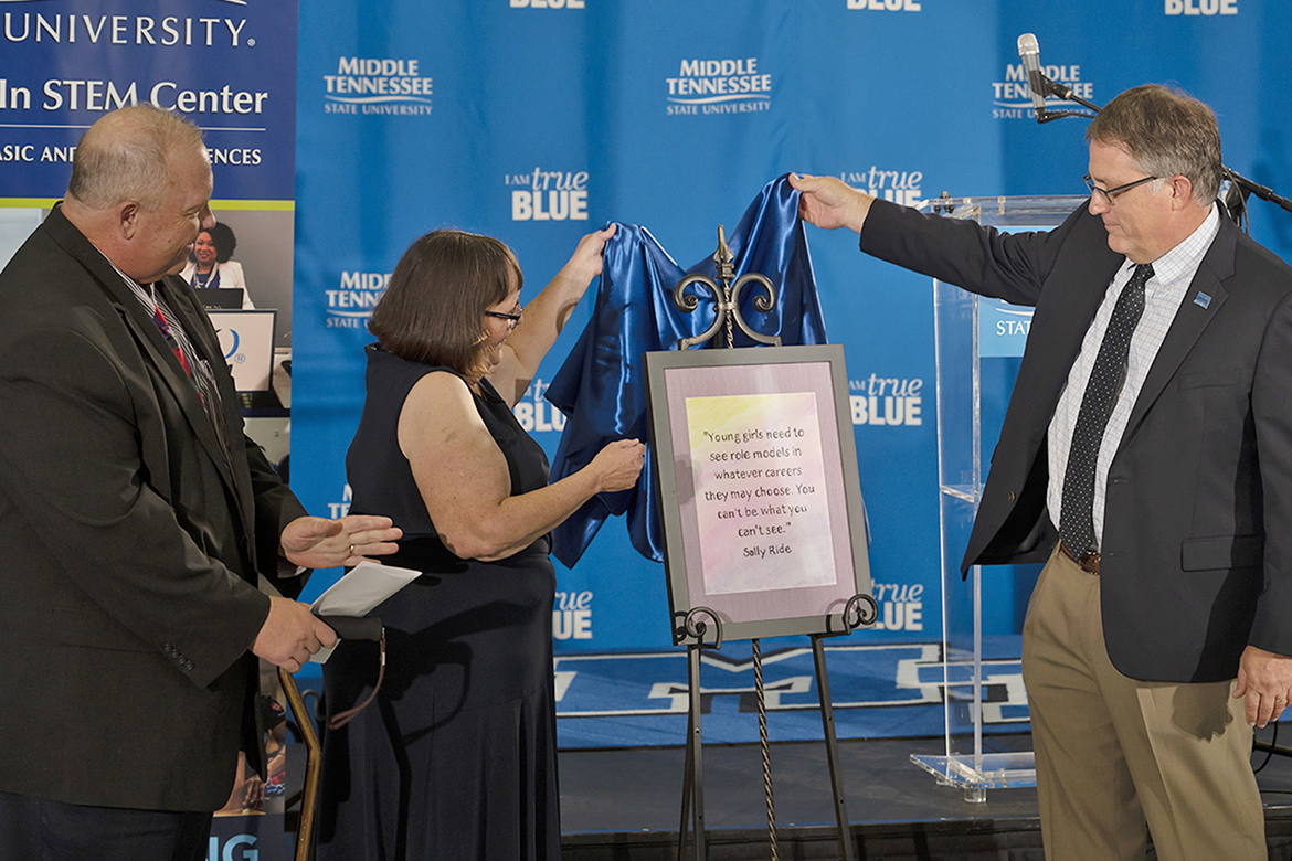 MTSU WISTEM Center Director Judith Iriarte-Gross, center, helps MTSU Provost Mark Byrnes, right, unveil a painting of a quotation by astronaut Sally Ride, created by artist Chrissie Richmond, during the 10th anniversary celebration for the WISTEM Center Wednesday, Oct. 9. College of Basic and Applied Sciences Dean Bud Fischer, left, expressed his appreciation for the center during the event. (MTSU photo by Cat Curtis Murphy)
