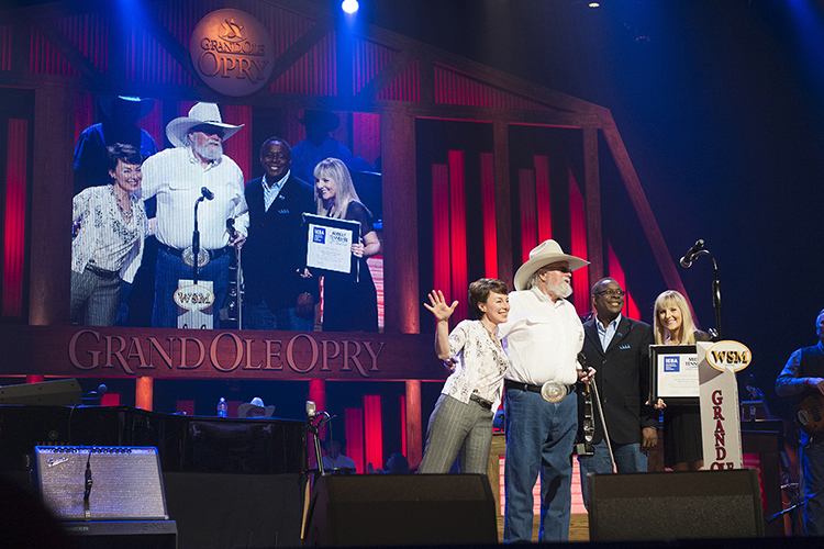 MTSU President Sidney A. McPhee, second from right, presents country music star Charlie Daniels with a framed announcement of the Charlie Daniels Scholarship at MTSU. Joining McPhee and Daniels on stage Saturday night at the Grand Ole Opry is Pam Matthews, left, executive director of the International Entertainment Buyers Association, and MTSU student Jordan Todd, a junior recording industry major, right. Daniels passed away Monday, July 6, at (MTSU file photo by Andy Heidt)