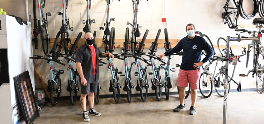 Bike shop employees, left, Elden Winkelman, and, right, David Candeto, pose in front of MTSU’s available rental bikes. (MTSU photo by Stephanie Barrette)