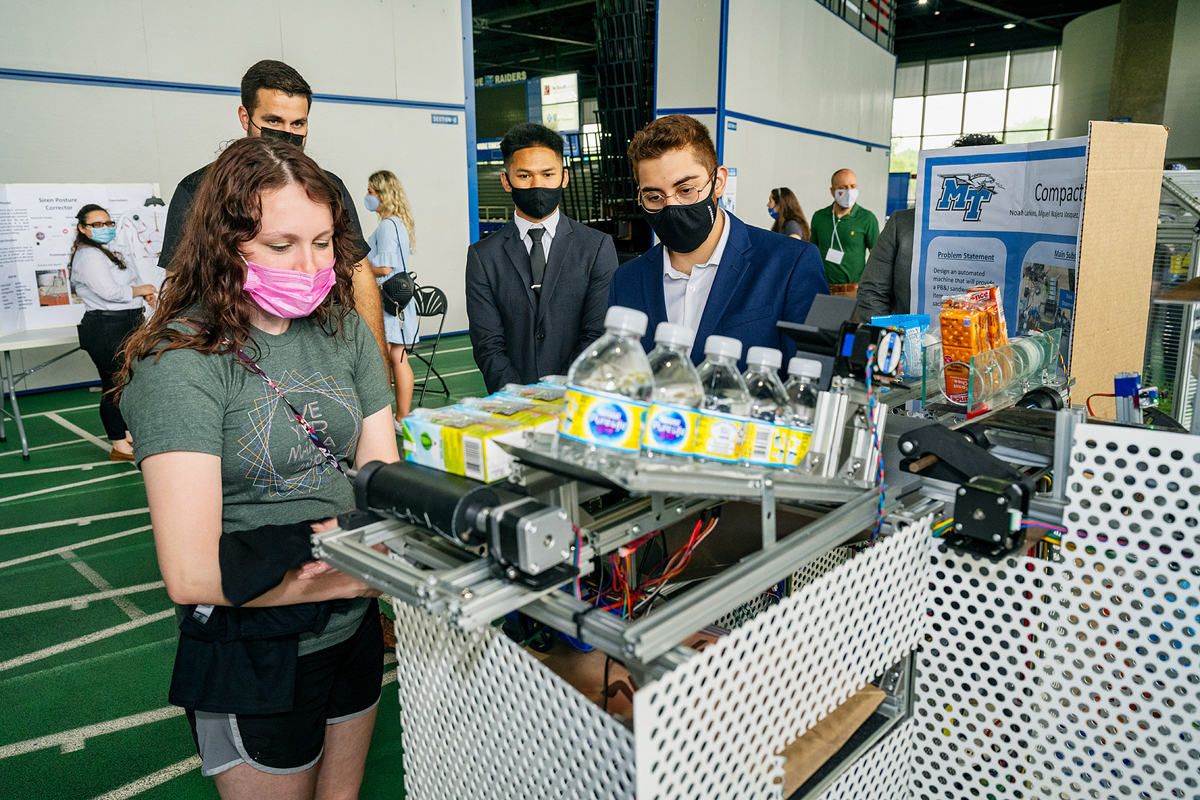 Hannah Davis, left, of Murfreesboro, left, waits for her food and beverage items to drop out of the “Compact Cafeteria” project as team member Jose Rubio explains how the technology works Thursday, April 29, during the annual MTSU Engineering Technology Mech-Tech Expo on the track level inside Murphy Center. The event showcased MTSU seniors’ projects. (MTSU photo by Andy Heidt)
