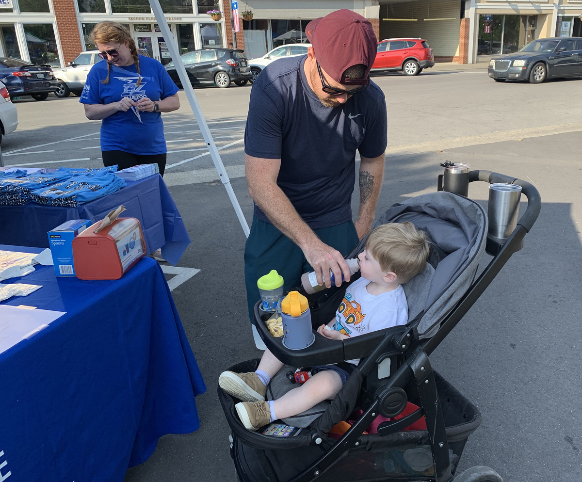 Lyndsey Bennett, left, checks out T-shirts for sale from the MTSU Dairy Science club while husband Greg Bennett gives 2-year-old Eddie Bennett a drink of MTSU Creamery chocolate milk May 22 during the first Main Street Saturday Market of the 2021 season in downtown Murfreesboro at the Historic Rutherford County Courthouse. The market, featuring MTSU Creamery milk products and ice cream, produce and other items, ends Oct. 30. (MTSU photo by Randy Weiler)