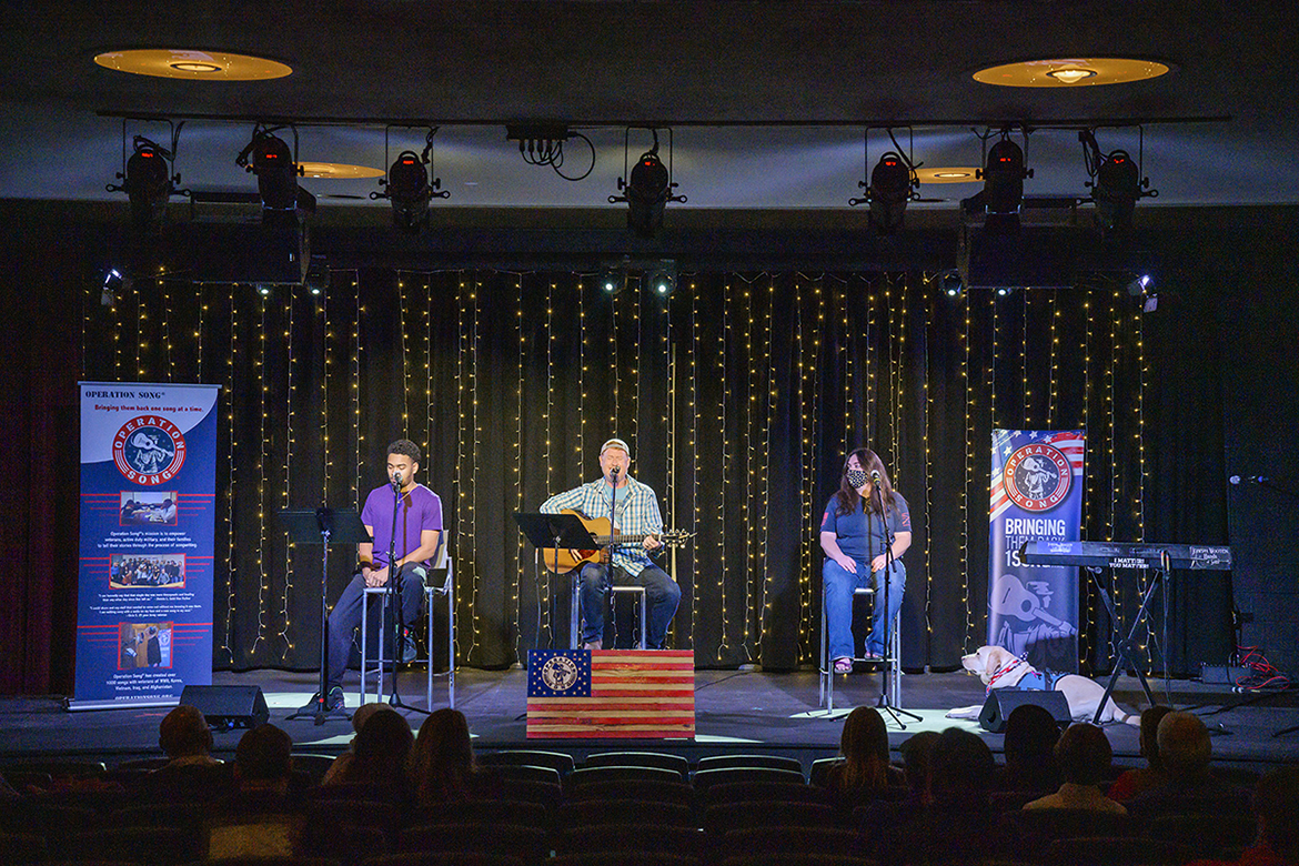 Leland the service dog shares the spotlight on stage in MTSU's Keathley University Center Theater with his owner, veteran Stefanie Marvin-Miller of Murfreesboro, right, an MTSU senior industrial/organizational psychology major while fellow MTSU senior Paul Mathews, left, a commercial songwriting major from Sherwood, Ark., sings their new co-written song, “Woman’s Best Friend,” with award-winning Nashville songwriter Adam Hood during the 2021 Operation Song retreat Oct. 29 at the university. The event teams trios of military veterans, student and professional songwriters to create healing music for the veterans and training for the students. (MTSU photo by Andy Heidt)