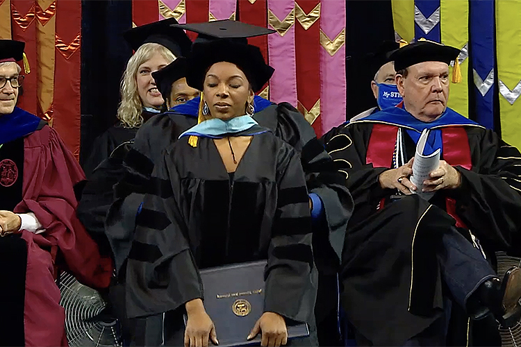 Brelinda Johnson, manager of the MTSU Scholars Academy in the Office of Student Success, kneels slightly as her adviser, Donald Snead, drapes her new doctoral hood across her shoulders Dec. 11 during MTSU’s Fall 2021 commencement in Murphy Center. Johnson earned the university’s first doctoral degree with a higher education concentration in MTSU’s Assessment, Learning and Student Success Program. (Screen capture from MTSU Livestream)