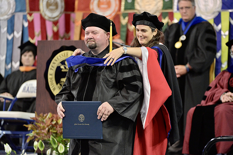 Middle Tennessee State University doctoral candidate Edward F. Beason of Livingston, Tenn., smiles as his adviser, MTSU digital history professor Molly Taylor-Poleskey, helps him don his new hood denoting his Ph.D. in public history Saturday, May 7, during the university's spring 2022 afternoon commencement ceremony in Murphy Center. MTSU awarded 2,474 degrees — 2,041 to undergraduates and 433 to graduate students — during its three-ceremony spring 2022 commencement event. (MTSU photo by Andy Heidt)