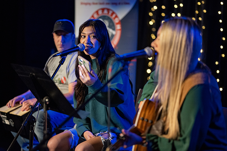 MTSU commercial songwriting major Katherine "Katt" Grimes, center, a senior and native of Lithia, Florida, who now lives in Murfreesboro, harmonizes with Kaitlyn Kilian, an Oklahoma songwriter, on "Roots," a song they co-wrote with student veteran Jeremy Barker, a Murfreesboro junior majoring in unmanned aircraft systems operations, who's listening in the background during the annual Operation Song writers' retreat at the university. The trio was one of seven who created and performed new songs in MTSU's Keathley University Center Theater at the Oct. 28 event. MTSU's Charlie and Hazel Daniels Veterans and Military Family Center and the Commercial Songwriting Program have hosted the event since 2016. (MTSU photo by Cat Curtis Murphy)