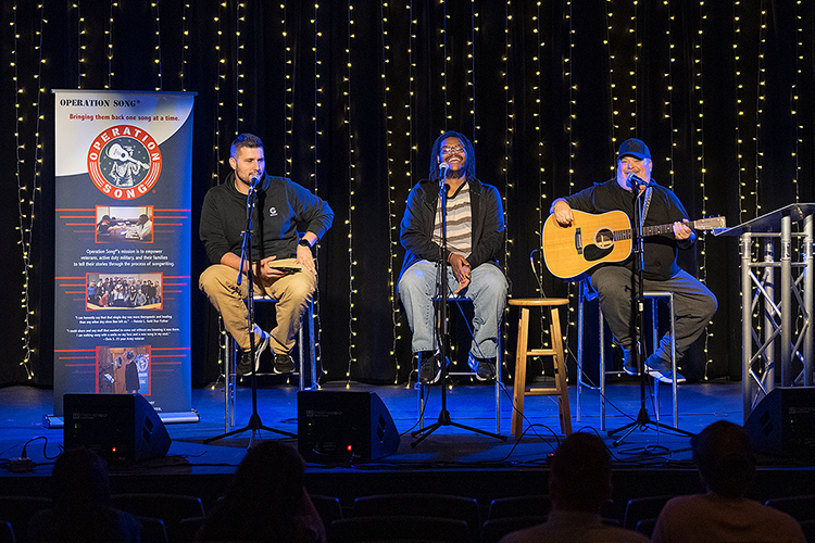 MTSU student veteran Jay Magruder of Murfreesboro, left, a senior majoring in unmanned aircraft systems operations, makes a point about "Honor Guard," a song composed from discussing his military service during the annual Operation Song writers' retreat at the university. Laughing and looking on before they perform the song in MTSU's Keathley University Center Theater Oct. 28 are his co-writers, senior commercial songwriting major Jaren Logan from Memphis, center, and professional songwriter Mark Irwin, a returning MTSU participant and songwriter for artists including Alan Jackson and Tim McGraw. MTSU's Charlie and Hazel Daniels Veterans and Military Family Center and the Commercial Songwriting Program have hosted the event since 2016. (MTSU photo by Cat Curtis Murphy)