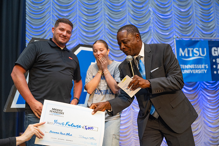 Taylor Kirouac, center, prospective Middle Tennessee State University student interested in studying marketing, receives a $5,000 scholarship from MTSU President Sidney A. McPhee, right, during the university’s kickoff event for the True Blue Tour at the Student Union Building on Wednesday, Sept. 13, 2023, in Murfreesboro, Tenn. At left by her side is father Jason Kirouac. (MTSU photo by Cat Curtis Murphy)