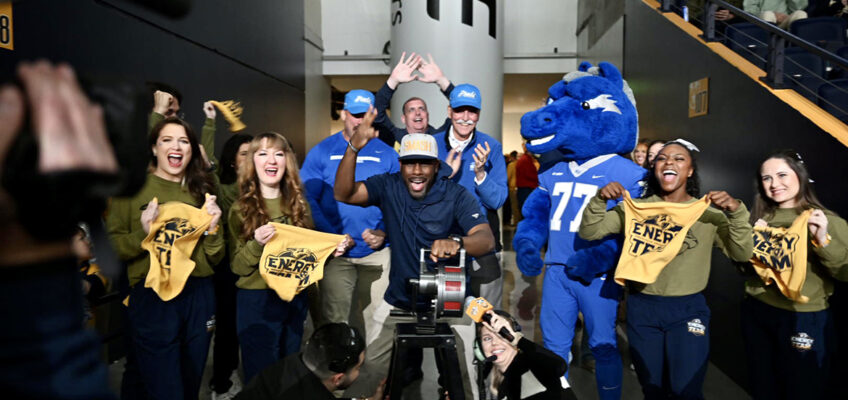 With cheerleading help, Derek Mason, center, Middle Tennessee State University Blue Raiders football coach, rides the elliptical machine during the Preds True Blue Night/Military Appreciation event during the NHL Nashville Predators' game March 19 against the San Jose Sharks at Bridgestone Arena in Nashville, Tenn. Mason served as a fan captain before the start of the game. (MTSU photo by James Cessna)