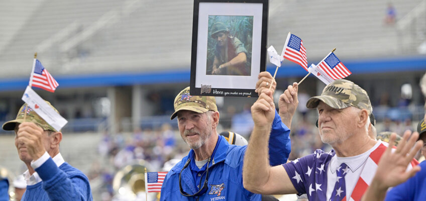 Middle Tennessee State University alumnus and U.S. Army Veteran Bob Lamb (Classes of 1969 and ’77), center, of Murfreesboro, Tenn., walks across Horace Jones Field in Floyd Stadium in Murfreesboro carrying a framed photo of his longtime friend and veteran, Bud Morris (’69, ’75)), Saturday, Nov. 9, during the 42nd annual MTSU Salute to Veterans and Armed Forces game during the halftime parade by service branches to theme songs performed by the Band of Blue. Morris, who attended the game, saluted his friends and fellow vets from the Jeff Hendrix Stadium Club, the first time in 40 years he has not walked with his military brothers and sisters. (MTSU photo by Andy Heidt)