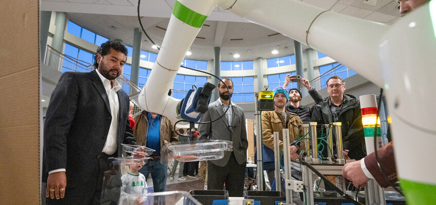 Emilio Sanches, left, and others watch as Kaleb Smith, right, turns on the FANUC-Cobit collaborative robotic arm for the “Meat Men: Thermoseal Meat Packager” team’s senior capstone project during the fall 2024 Mech-Tech event Dec. 5 in the Miller Education Center on Bell Street in Murfreesboro, Tenn. (MTSU photo by Cat Curtis Murphy)