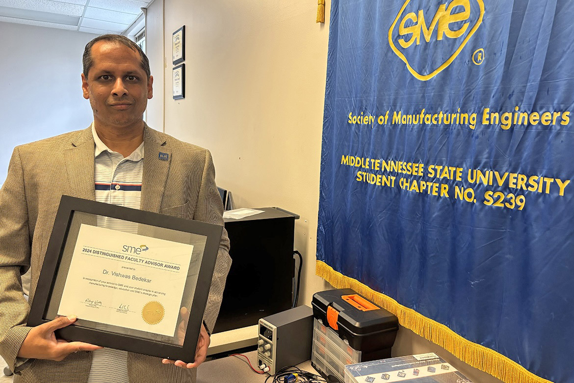 In the Voorhies Engineering Technology laboratory beside the Society of Manufacturing Engineers student chapter banner on the Middle Tennessee State University campus in Murfreesboro, Tenn., MTSU Engineering Technology associate professor Vishwas Bedekar holds the certificate he received for being selected one of eight SME Distinguished Faculty Advisor national award winners for 2024. An award-winning robotics mentor, Bedekar earned the same honor in 2022. (MTSU photo by Randy Weiler)