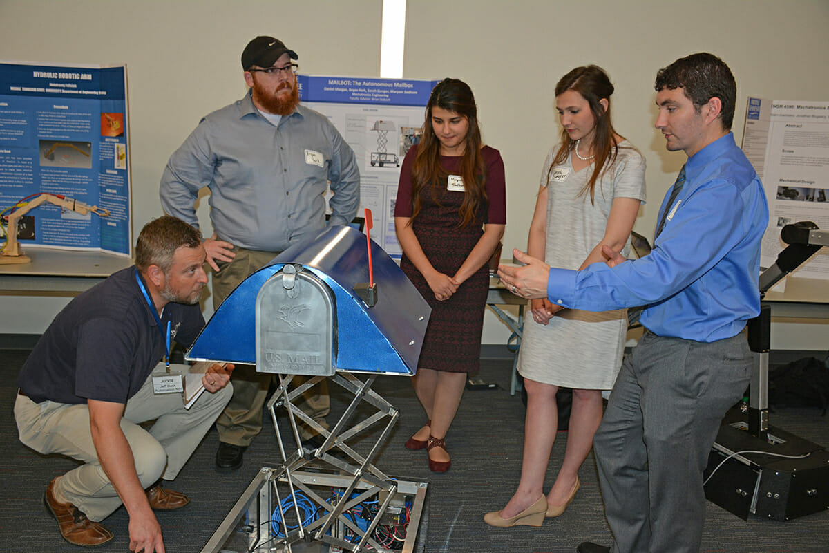 Competition judge Jeff Buck, kneeling, of Automation Nth, listens as MTSU senior Daniel Morgan, right, answers Buck's question about the "Mailbot" during the Department of Engineering Technology Poster and Project Presentation at the Nissan Training Center in Smyrna, Tenn., in April 2017. Other mechatronics engineering team members include, from left, Bryan York, Maryam Sedhom and Sarah Gunger. This year’s open house is set April 26 from 3 to 5 p.m. (MTSU file photo by Randy Weiler)