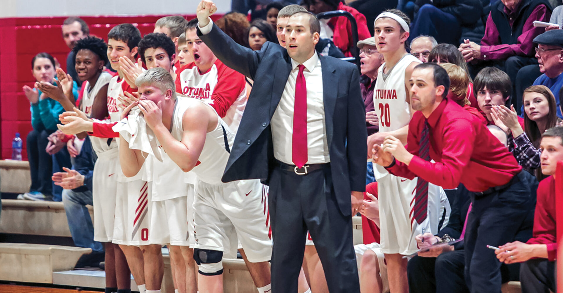 Kevin Kanaskie shoves his fist in the air as her coaches a high school basketball team. All around him, fans cheer and the team applauds.
