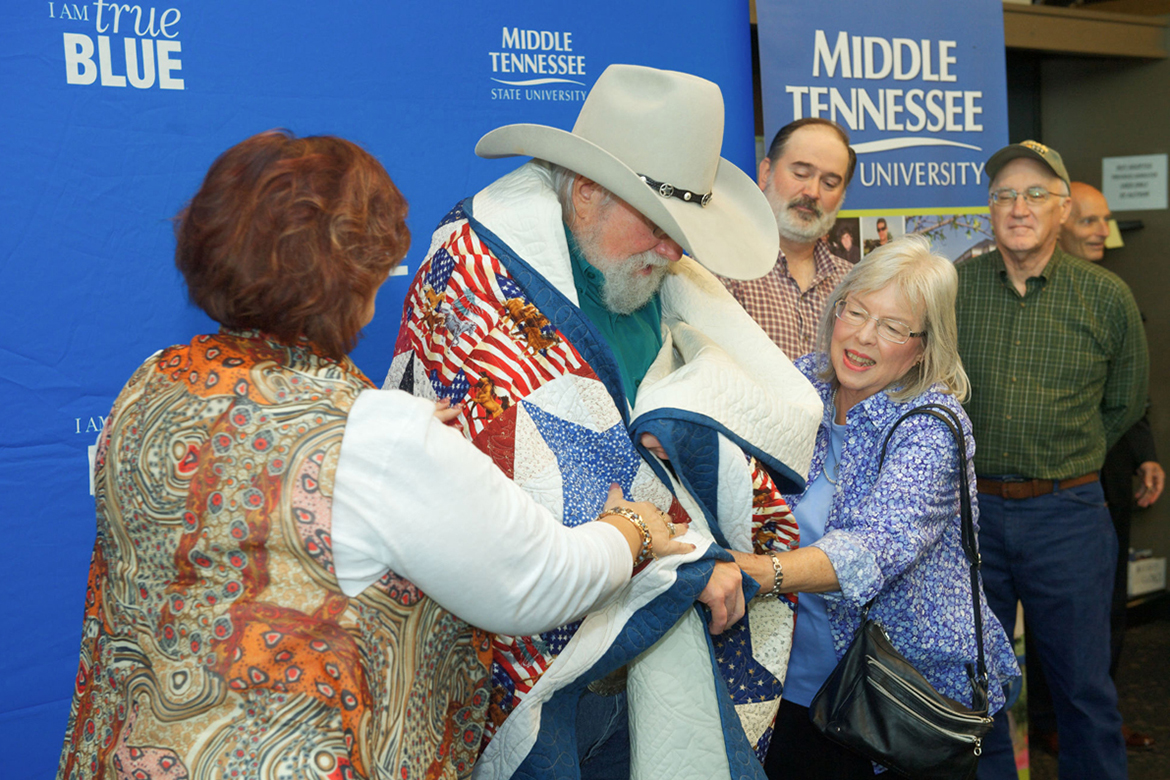 Mary Gross, left, and Jill Shaver, right, part of the local Quilts of Valor organization, place a quilt they made around famed entertainer Charlie Daniels Thursday, Nov. 2, while he was at MTSU signing copies of his memoir at Phillips Bookstore. (MTSU photo by Andy Heidt)