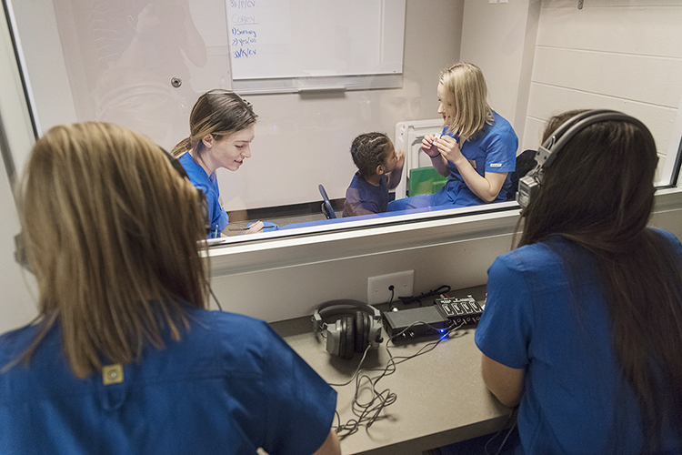 MTSU student clinicians Kali Elliott, left, and Corey Lawson, right, work with client Malachi McCord in the background as students Kelsey Armstrong and Dayna LaRoue observe from the other side of the glass at the MTSU Speech-Language-Hearing Clinic. The clinic is celebrating its 50th anniversary with a move to a new home in the Alumni Memorial Gym. (MTSU photo by Andy Heidt)