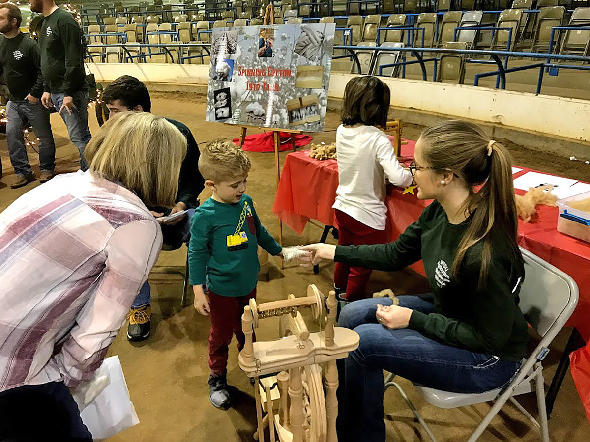 MTSU School of Agriculture student Rachel Elrod, right, shows a small child a small piece of cotton she had spun on the spinning wheel and gave it to the youngster during the Christmas Village.