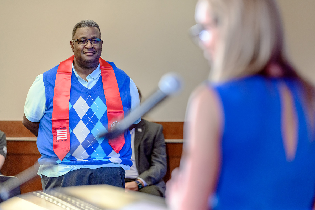 Derrick Wharton, left, of Murfreesboro, Tenn., listens as Daniels Veterans Center Director Hilary Miller shares information about him with the audience attending the in-person Graduating Veteran Stole Ceremony Wednesday, April 28, in the Sam Ingram Building’s MT Center. A detective with MTSU’s Police Department, Wharton served in the U.S. Navy and resumed college several years ago at MTSU after his daughter graduated from high school. (MTSU photo by J. Intintoli)
