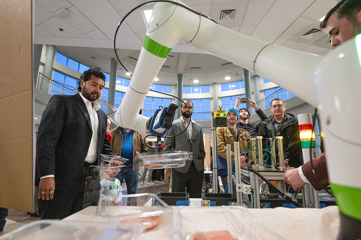 Emilio Sanches, left, and others watch as Kaleb Smith, right, turns on the FANUC-Cobit collaborative robotic arm for the “Meat Men: Thermoseal Meat Packager” team’s senior capstone project during the fall 2024 Mech-Tech event Dec. 5 in the Miller Education Center on Bell Street in Murfreesboro, Tenn. (MTSU photo by Cat Curtis Murphy)
