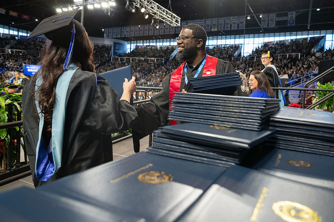 Chris Rochelle, right, assistant director of the Charlie and Hazel Daniels Veterans and Military Family Center, hands out diploma covers to graduates during the fall 2025 commencement morning ceremony held Saturday, Dec. 13, in Murphy Center on the MTSU campus in Murfreesboro, Tenn. (MTSU photo by Cat Curtis Murphy)