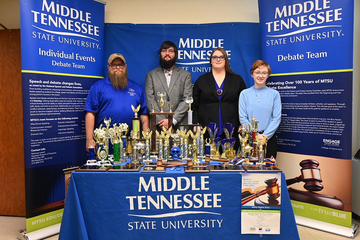 Patrick Richey, left, communication studies associate professor and MTSU Debate Team coach, is pictured inside Jones Hall at Middle Tennessee State University with Blue Raider Debate members Derek Dismukes, a spring graduate in criminal justice administration and pre-law minor; rising senior Jessica Rogers, a psychology and communication studies major; and Elliot Certain, a rising senior social work major with an honors minor, with the collection of trophies and awards captured by individual members and the team during the 2022-23 debate season. (MTSU photo by Jimmy Hart)