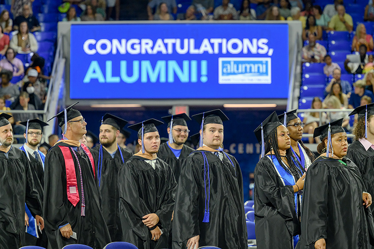 With a congratulatory digital sign in the background, proud Middle  State University graduates make their way to their seats inside Murphy Center for the Summer 2023 commencement ceremony. (MTSU photo by J. Intintoli)