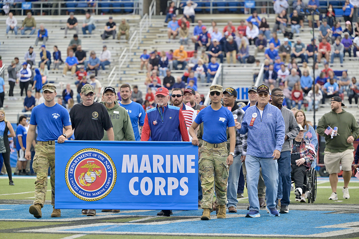 Led by Middle Tennessee State University ROTC cadets Matthew Chappell, left, and George Jouny carrying the U.S. Marine Corps banner, a group of Marine veterans go across Horace Jones Field in Floyd Stadium while the Band of Blue performs their theme song, “The Marines’ Hymn,” in November 2024, as part of 42nd annual Salute to Veterans and Armed Forces game activities on the campus in Murfreesboro, Tenn. All U.S. military branches will go across the field during halftime ceremonies for the 43rd annual Salute to Veterans game on Saturday, Nov. 8. (MTSU file photo by Andy Heidt)