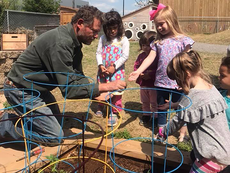 Children at MTSU's Ann Campbell Early Learning Center wait their turns and help local entertainer, farmer and dad "Cowboy Dan," left, check on their vegetables in the raised garden beds at the center's wheelchair-accessible natural playground in this 2018 file photo. The ACE Center is part of the Early Learning Programs in MTSU's College of Education, which is offering a new online version of a course for preschool educators to help very young children develop social and emotional skills. (MTSU file photo by Jacob Smith/Ann Campbell Early Learning Center)