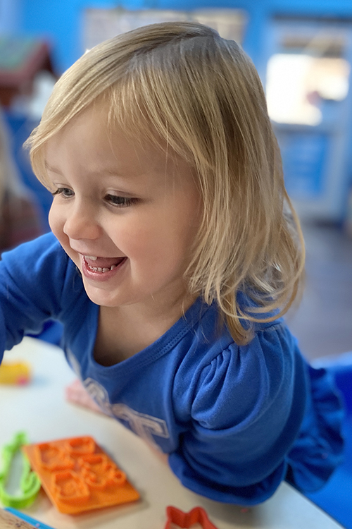 One of the little learners at MTSU's Ann Campbell Early Learning Center, wearing her blue "MT Raiders" shirt, grins as she tries to decide which shape to cut out next in play dough in the center's Blue Room for 2- and 3-year-olds. The nonprofit, inclusive preschool, an arm of MTSU’s College of Education, is holding a drive-thru version of its annual "Saddle Up" fundraiser on Saturday, April 17. For more information, visit https://www.mtsu.edu/acelearningcenter/saddleup.php. (Photo courtesy of the Ann Campbell Early Learning Center at MTSU)