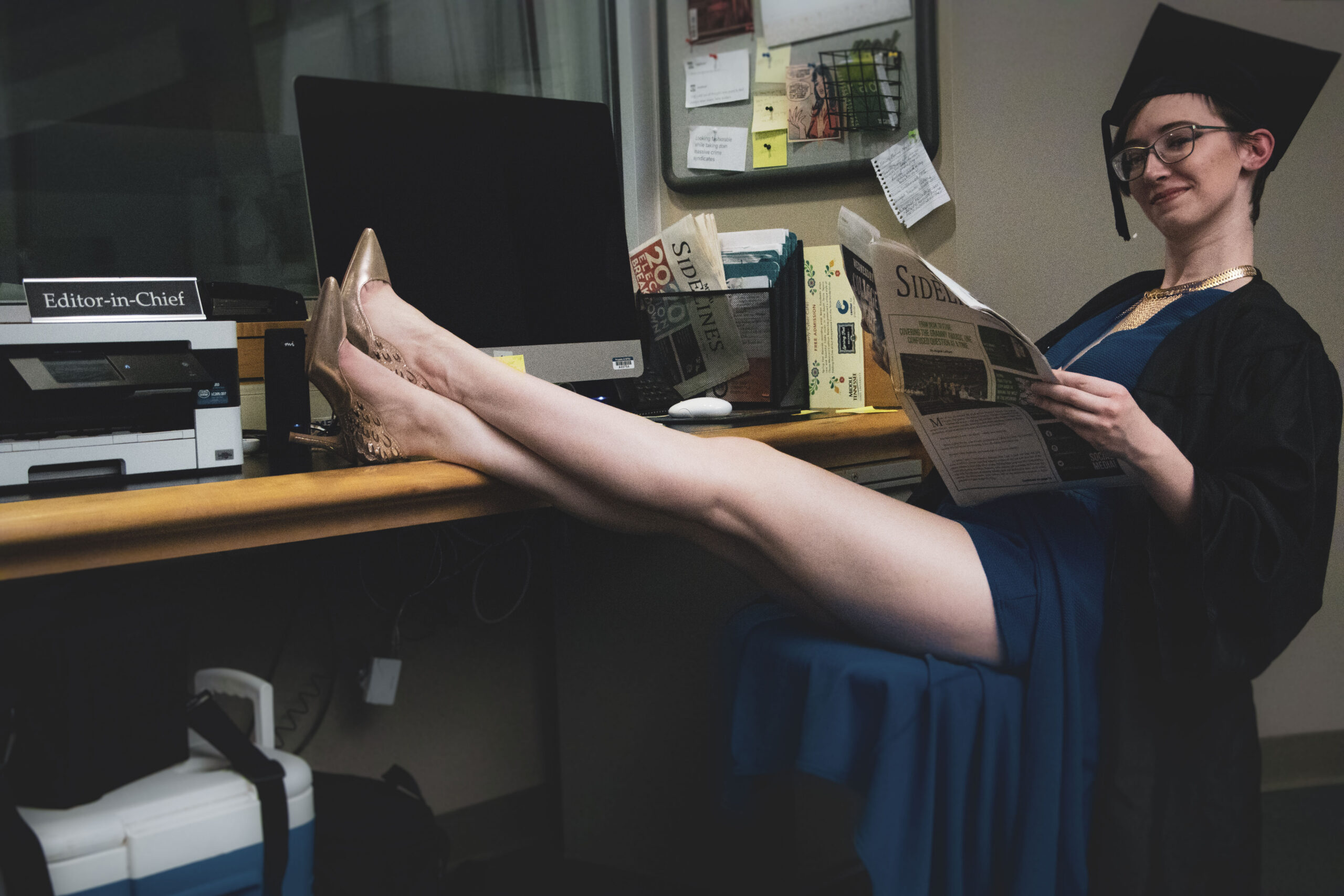 Student Angele Latham sits at her news desk holding a newspaper. 