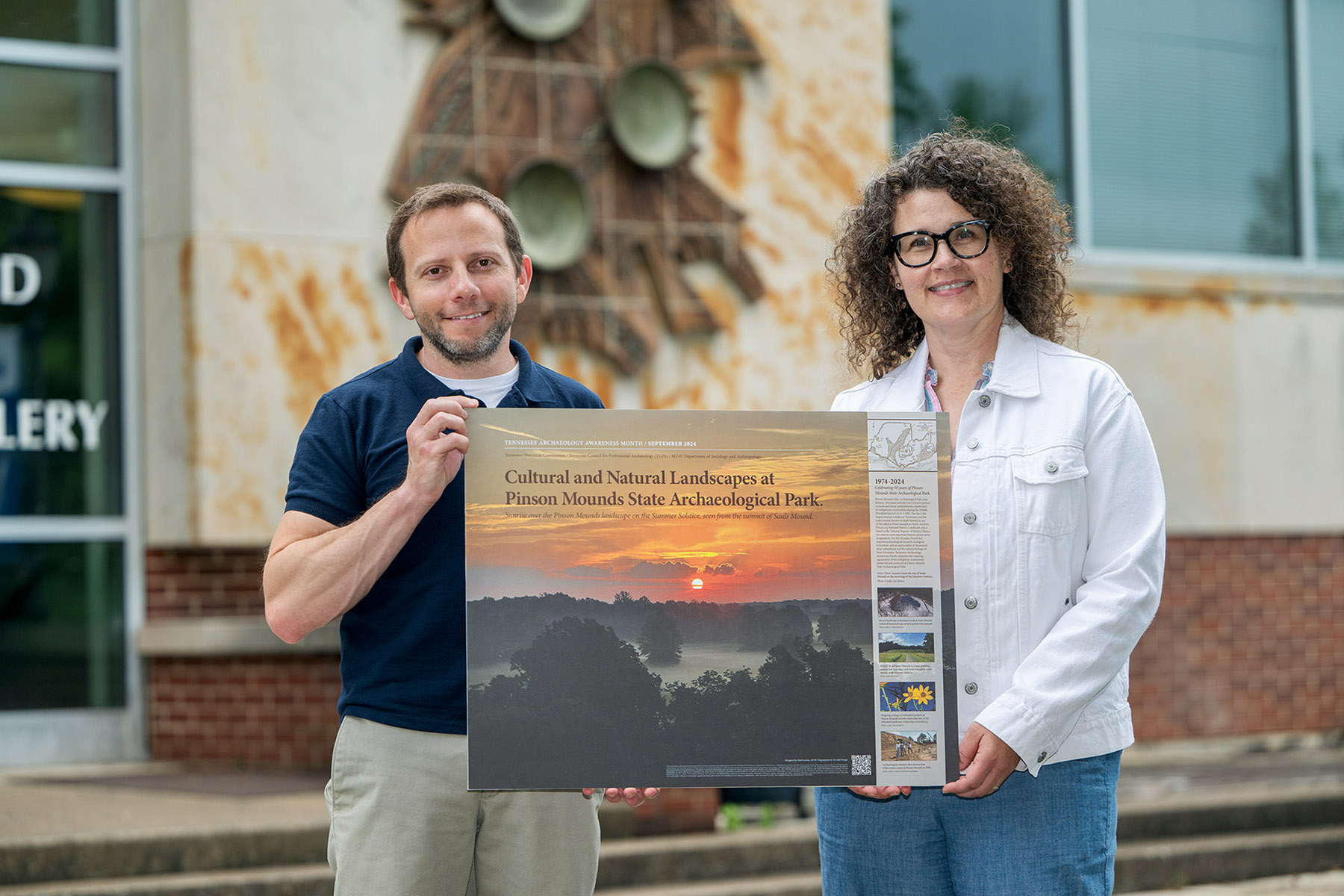 Noel Lorson, associate professor in the Department of Art and Design at Middle Tennessee State University in Murfreesboro, Tenn., at right, holds her winning design for the Society for American Archaeology’s 2025 Archaeology Awareness Month poster contest alongside fellow collaborator Paul Eubanks, associate professor of anthropology in the MTSU Department of Sociology and Anthropology, in front of Todd Hall on campus. (MTSU photo by Andy Heidt)