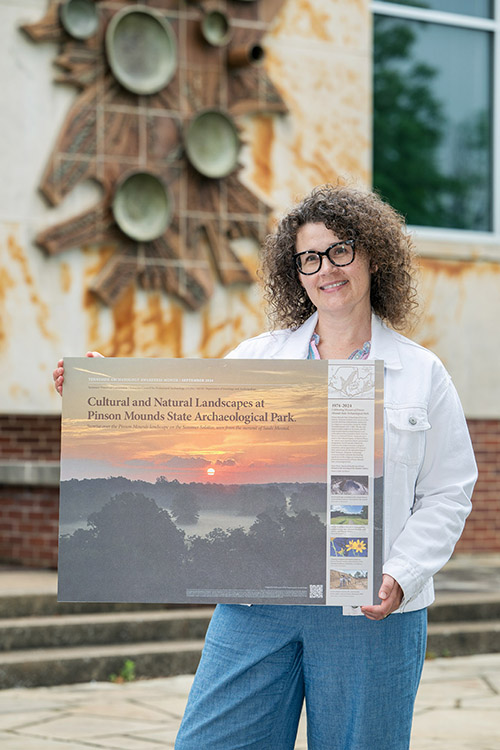 Noel Lorson, associate professor in the Department of Art and Design at Middle Tennessee State University in Murfreesboro, Tenn., at right, holds her winning design for the Society for American Archaeology’s 2025 Archaeology Awareness Month poster contest. The design features Pinson Mounds State Archaeological Park, a large complex of prehistoric Native American mounds located in West Tennessee. (MTSU photo by Andy Heidt)