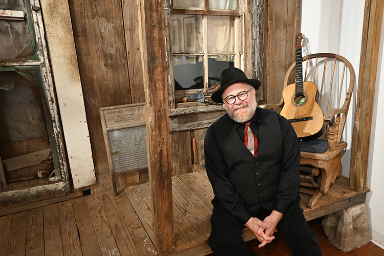 Photojournalist and MTSU alumnus Bill Steber sits on the porch of a facade of a salvaged Mississippi Delta sharecropper's shack that is part of his exhibit, "Deep Roots: Evocations of the Mississippi Delta Blues," on display through Dec. 9, 2023, in Middle Tennessee State University's Baldwin Photographic Gallery. (MTSU photo by Nancy DeGennaro)