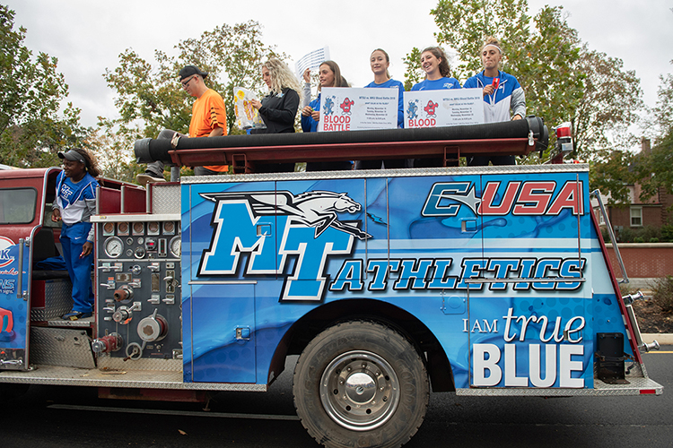 Student volunteers, led by Chelsea Floyd, left, MTSU assistant athletic director for marketing, wave banners and toss candy from a customized antique fire truck at the 2019 homecoming parade to reach hundreds of university supporters and encourage crowds to "Bleed Blue, Beat WKU" during the annual blood drive competition Monday-Wednesday, Nov. 18-20. The event will be held at the Campus Recreation Center gym, 1848 Blue Raider Drive, from 11 a.m. to 6 p.m. each day. You can make an appointment today at http://bit.ly/MTSUBleedBlue2019. (MTSU photo by James Cessna)