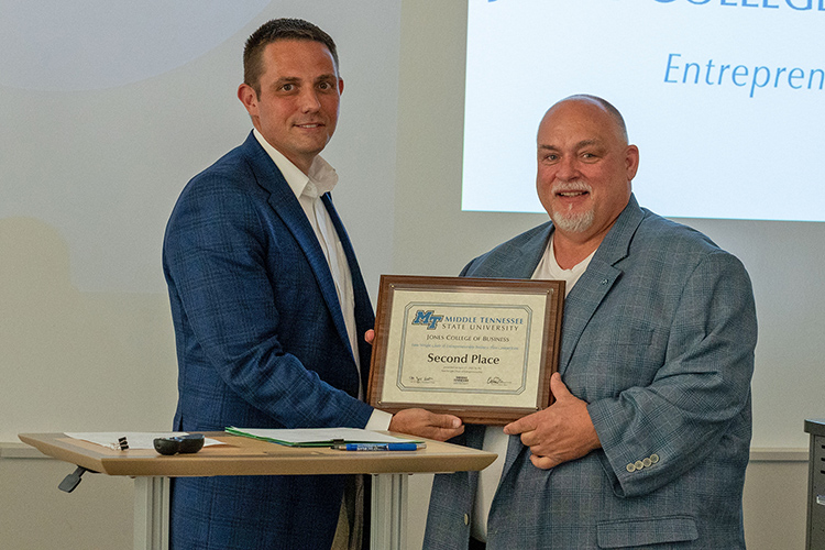 Billy Fryar, a senior entrepreneurship major from Chattanooga, Tennessee, is presented the second-place plaque and $6,000 prize from Joshua Aaron, management professor and holder of the Wright Chair of Entrepreneurship, at the conclusion of the 2022 Business Plan Competition Finals held April 27 in the Academic Classroom Building. The event is presented by the Pam Wright Chair of Entrepreneurship within the Department of Management. Fryar won for his proposal for his company, 911tarp.com, which provides emergency tarp services to protect homeowners’ property following damaging storms. (MTSU photo by Darby Campbell-Firkus)