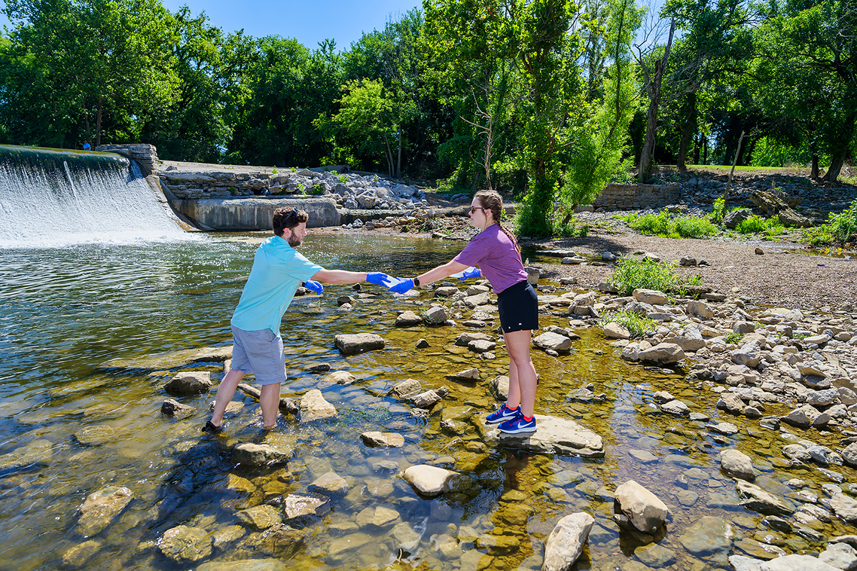 MTSU biology research assistant professor Cole Easson, left, hands rising senior Jacqueline Williams of Drummonds, Tenn., a plastic bottle of water he took from the Stones River at the Walter Hill Dam in Murfreesboro. They will map aquatic diversity using next-generation sequencing techniques relative to land use in the surface waters in the river at 10 locations across the area. (MTSU photo by Andy Heidt)