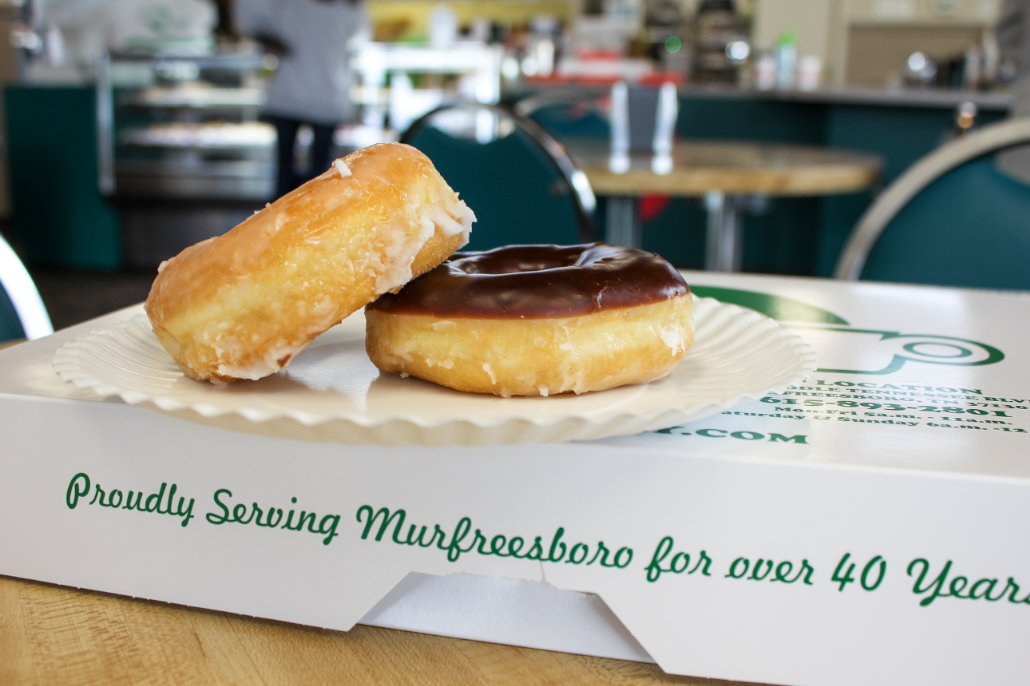 A glazed donut and chocolate donut on top of a Donut Country box in Donut Country's dining room