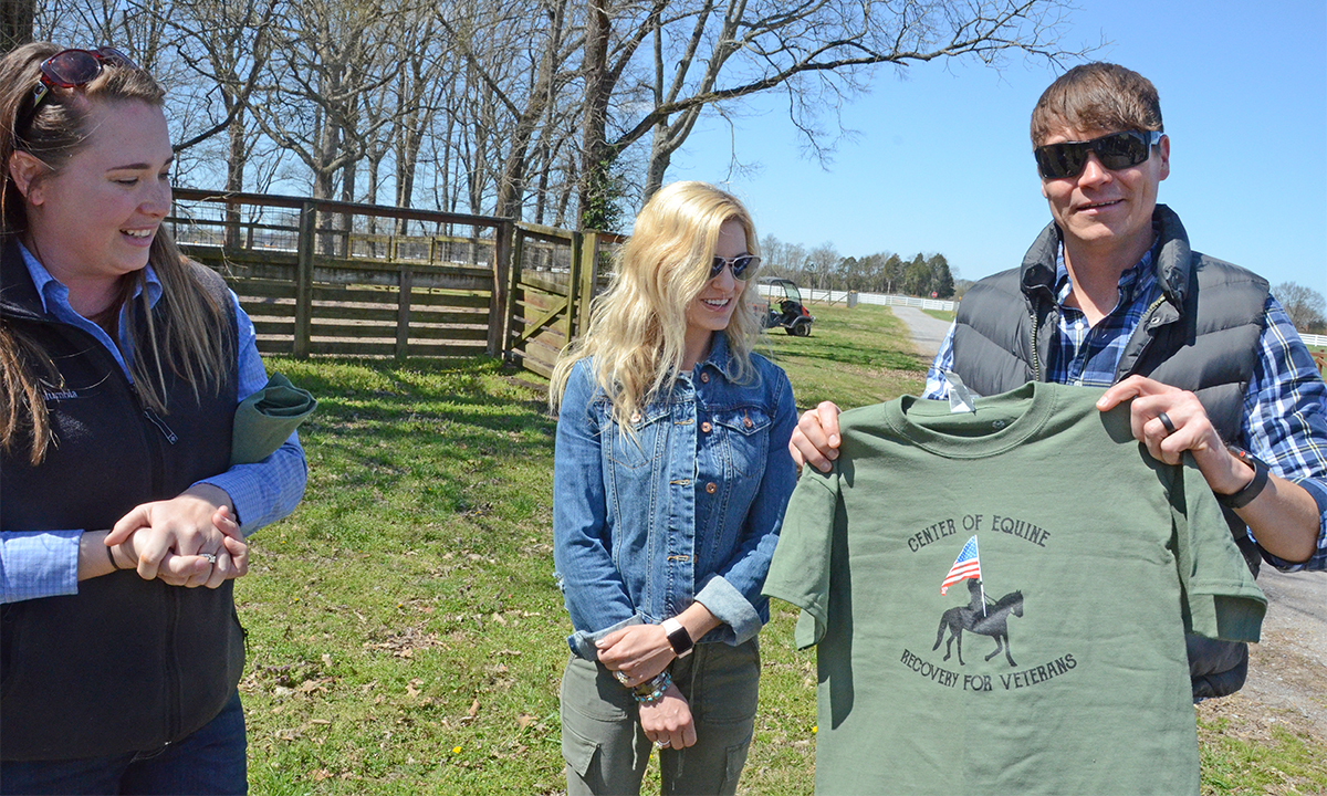 Andrea Rego, left, an MTSU horse science instructor and coordinator of the Center of Equine Recovery for Veterans program to assist with equine therapy for veterans, presents Brad Arnold with a CERV T-shirt as his wife, Jen Arnold, watches outside the Horse Science Center on West Thompson Lane. The Arnolds delivered a $15,000 check for the equine therapy center from the rock band 3 Doors Down’s Better Life Foundation. 