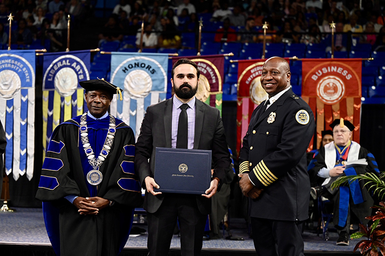 Metro Nashville Police Department detective Zachary Plese, center, holds his honorary professorship in public safety certificate presented by MTSU President Sidney A. McPhee, left, at the university’s spring commencement ceremony Friday, May 5, in Murfreesboro, Tenn. At right is Metro Nashville Police Chief John Drake. A total of five officers received the honor for their heroic response to the Covenant School shooting in Nashville, Tenn., in late March. (MTSU photo by James Cessna)