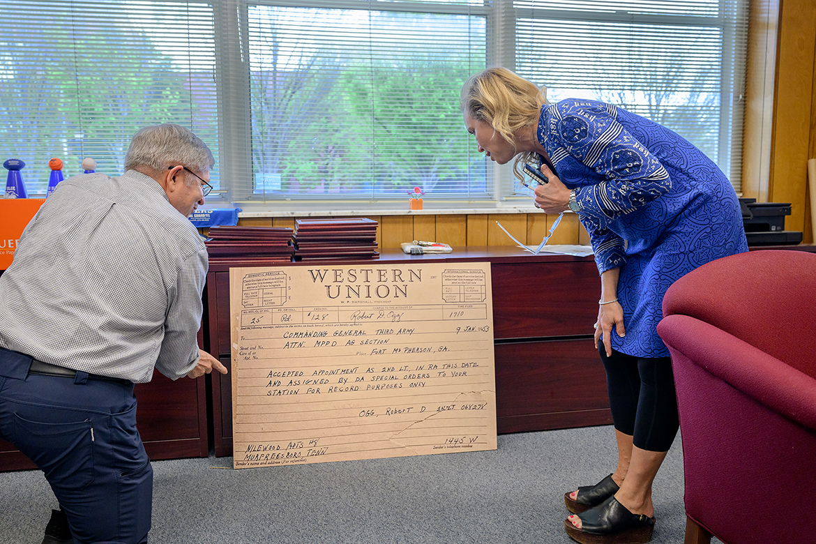 Rickey Smith, left, a Middle Tennessee State University alumnus and retired U.S. Army colonel, and Hilary Miller, director of the MTSU Charlie and Hazel Daniels Veterans and Military Family Center on campus in Murfreesboro, Tenn., look at a large replica of a Western Union telegram the U.S. Army sent in 1953 to Robert Ogg, the first MTSU cadet when the program began in 1950 and first to be commissioned as a second lieutenant, explaining his orders to go to Fort McPherson, Ga. Shown in the Department of Military Science office, the telegram will be on display Thursday, April 10, during the 75th anniversary celebration for the MTSU ROTC program — an event open to the public and to be held outdoors, weather permitting, at the Veterans Memorial site outside the Tom H. Jackson Building, 628 Alma Mater Drive. (MTSU photo by J. Intintoli)