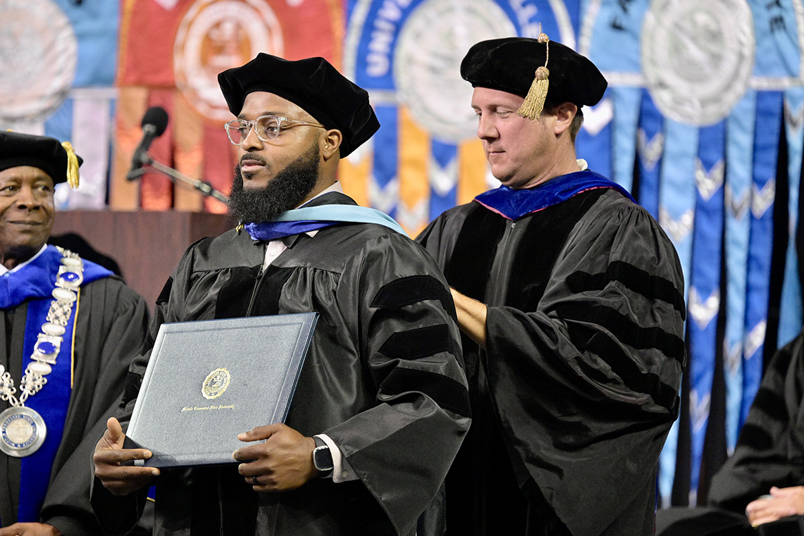 Middle Tennessee State University graduate David M. Cowan is hooded by his major professor, Kevin Krahenbuhl, upon receiving his doctoral degree in education during the summer 2025 commencement ceremony held Saturday, Aug. 9, inside Murphy Center on campus in Murfreesboro, Tenn. At far left is MTSU President Sidney A. McPhee. (MTSU photo by Andy Heidt)