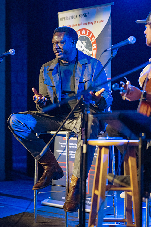 MTSU student veteran Bennie Thompson Sr. of Fayetteville, Tennessee, a junior majoring in concrete industry management major, explains what went into "Sand and Smoke," a song composed from discussing his military service during the annual Operation Song writers' retreat at the university. Looking on before they perform the song in MTSU's Keathley University Center Theater Oct. 28 is one of his co-writers, senior commercial songwriting major Ryan Haynes of Sterrett, Alabama. Professional songwriter David Kent, who isn't shown, was the third member of the trio, whose partnership stunned the audience with the song's changing visions of home and war. MTSU's Charlie and Hazel Daniels Veterans and Military Family Center and the Commercial Songwriting Program have hosted the event since 2016. (MTSU photo by Cat Curtis Murphy)