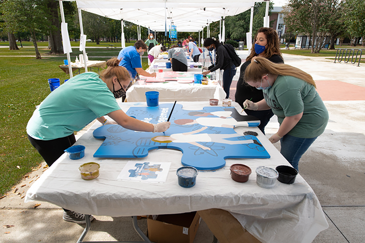 MTSU students, faculty and staff paint oversized wooden puzzle pieces representing interdisciplinary core skills, including one for "people management," shown in the foreground, during an outdoor "Pop-Up Mural Event" in September on campus. The 10 different handcrafted puzzle pieces, now ready again for display, are part of a public art project collaboration between the College of Liberal Arts and the College of Basic and Applied Sciences to show students the skills they need for success. (MTSU photo by James Cessna)